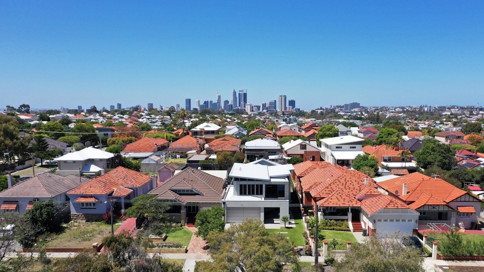 Aerial view of suburban Australian housing with Perth city skyline in the background, illustrating urban density and residential property markets.
